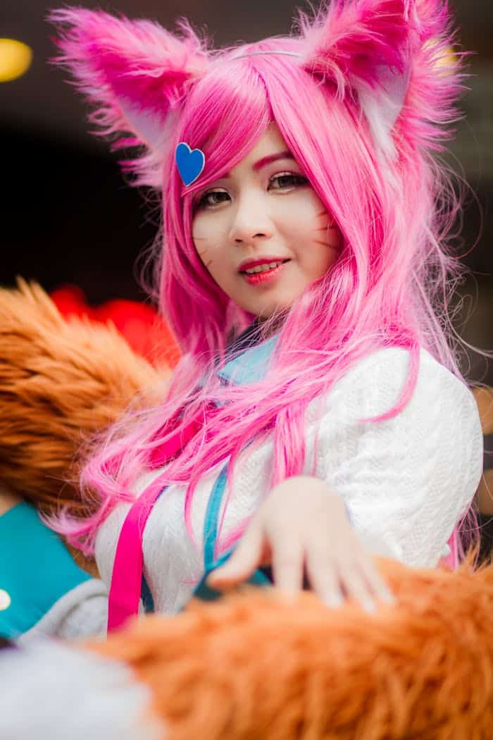 A colorful cosplay character with pink hair and fox ears, posing playfully.